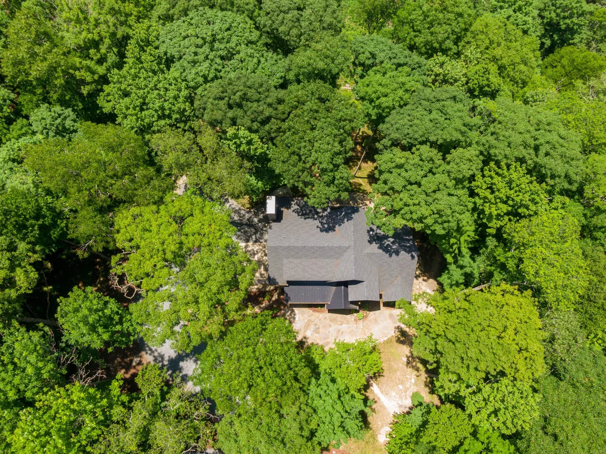 A broad exterior angle capturing the house nestled among tall trees with a spacious driveway, evoking a sense of peaceful seclusion. The porch and surrounding forest affirm the property’s connection to the outdoors.