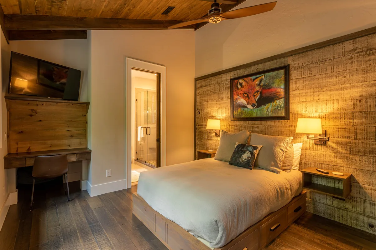 A welcoming bedroom with a bed featuring soft linens, a whimsical fox painting above the headboard, a wooden desk and chair for work, and an adjacent bathroom door. The room is both functional and artistic, offering a comfortable place to relax or get work done.