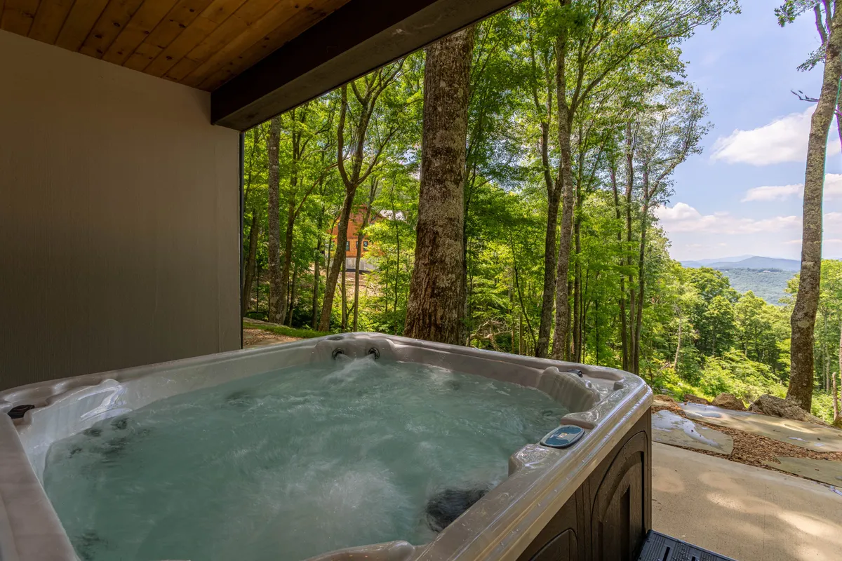 A tranquil outdoor patio with a private hot tub set against a scenic mountain backdrop, surrounded by natural greenery, creating a rejuvenating retreat perfect for soaking and stargazing.