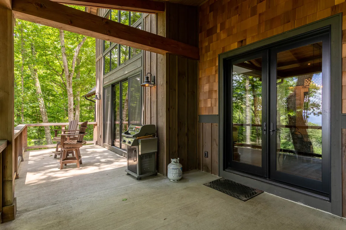 An inviting wooden deck with outdoor seating and a grill, accessed through large glass doors, is nestled amongst greenery. The scene hints at relaxation after active adventures—perfect for unwinding, barbecuing, or gathering with friends while enjoying the outdoors.