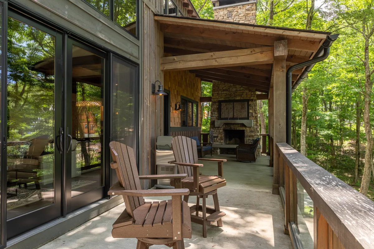 This image captures a beautiful outdoor deck area featuring wooden chairs arranged around a striking stone fireplace, all surrounded by lush greenery. The cozy seating and natural stone elements emphasize the inviting atmosphere and direct connection to the outdoors, perfectly embodying the deck's role as an extension of nature.