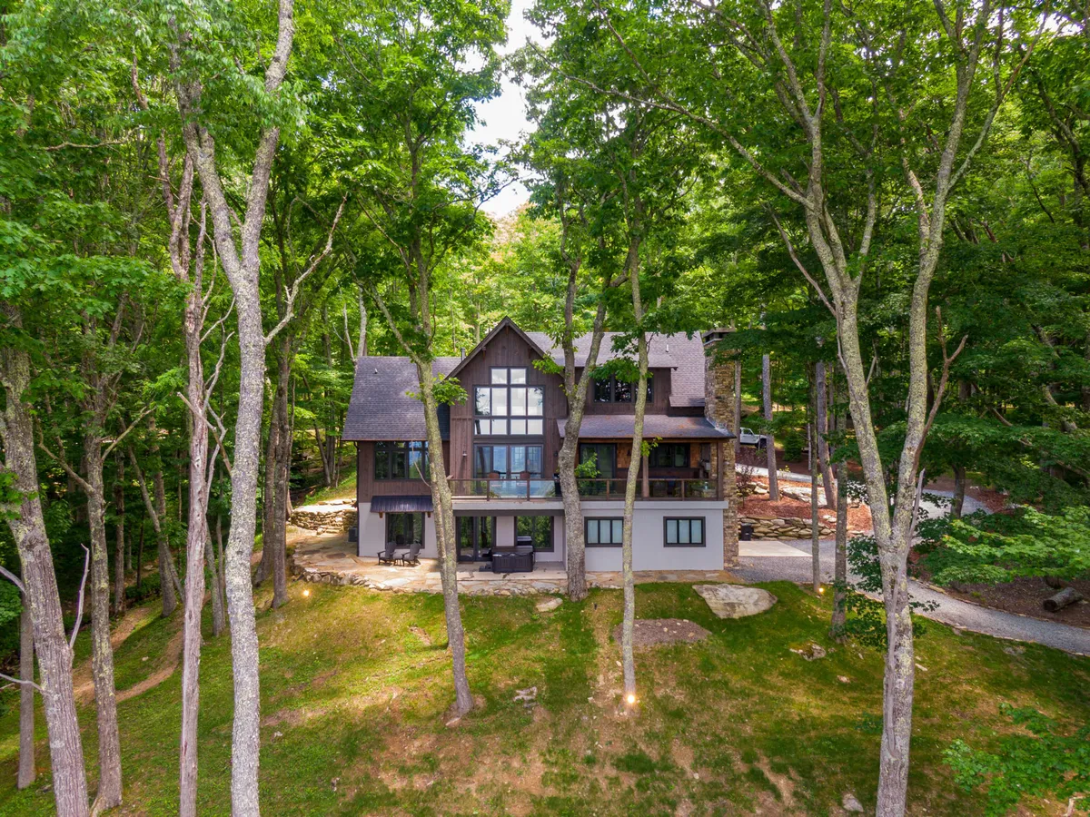 An exterior view emphasizing the lodge’s modern design, large windows, patio area, and the surrounding trees. The space is set up for outdoor gatherings, nature walks, and stargazing, with a peaceful and inviting ambiance.