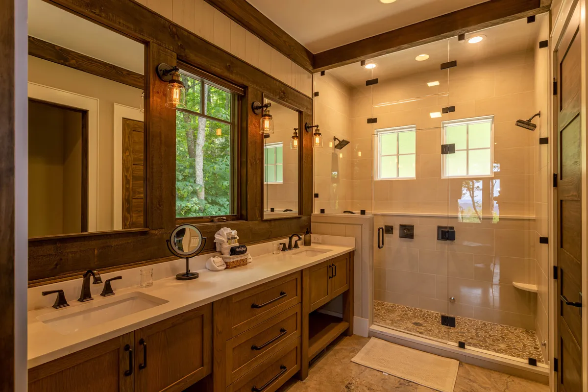 A spa-inspired bathroom with a double sink vanity, walk-in shower, abundant natural light from windows, and stylish wooden accents. The space is bright, serene, and thoughtfully designed for relaxation and self-care routines.
